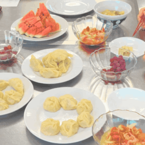 モンゴルの家庭料理のスープや、包子（ヴォーズ）やサラダ、スイカ、ブドウなどが乗っているテーブルの様子