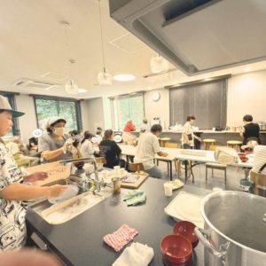 ネオアス村地域食堂で食事や会話を楽しむ利用者さんたちと、配膳やお皿洗などをするボランティアさんたちの様子