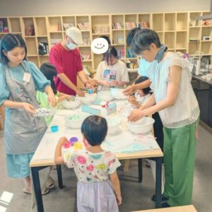 バスボム作りを教えている学生ボランティアと、楽しそうにバスボムを作る参加者さんたちの様子