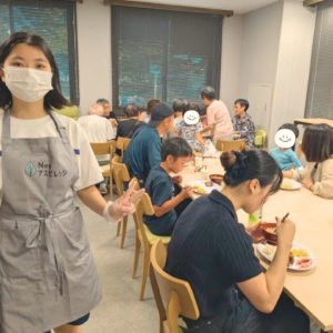 配膳を行う学生ボランティアと、ネオアス村地域食堂で会話や食事を楽しむ参加者さんたち