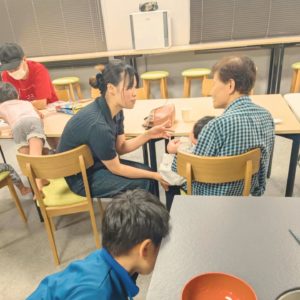 赤ちゃんと抱っこする年配の女性と、赤ちゃんのお母さんが椅子に座って話している様子