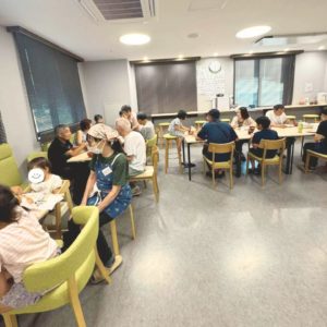 ネオアス村地域食堂でしょくじや会話をする参加者さんと、小さい子どもに食事の介助をする女性ボランティアの様子
