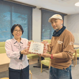 ネオアス村地域食堂に、ヤクルトの寄付を届けてくれた新潟中央ヤクルトの女性従業員さんとNeoアスビレッジ理事長がカメラに向かって笑顔を見せている様子