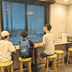 ネオアス村地域食堂のカウンターに座って会話をする3人の男の子の様子