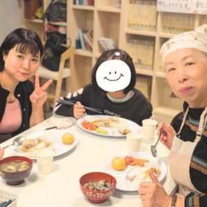 食事をしながらカメラに向かって笑顔を向ける2名の女性と1人の子どもの様子