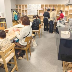 ネオアス村地域食堂で食事や会話をする親子と盛り付けや配膳を行うボランティアさんたちの様子