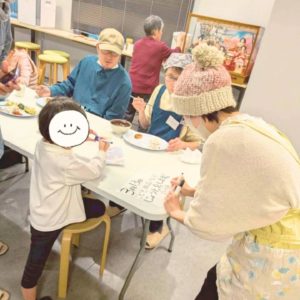 お知らせの看板を書いている女性ボランティアと、それを見ている幼稚園生の様子